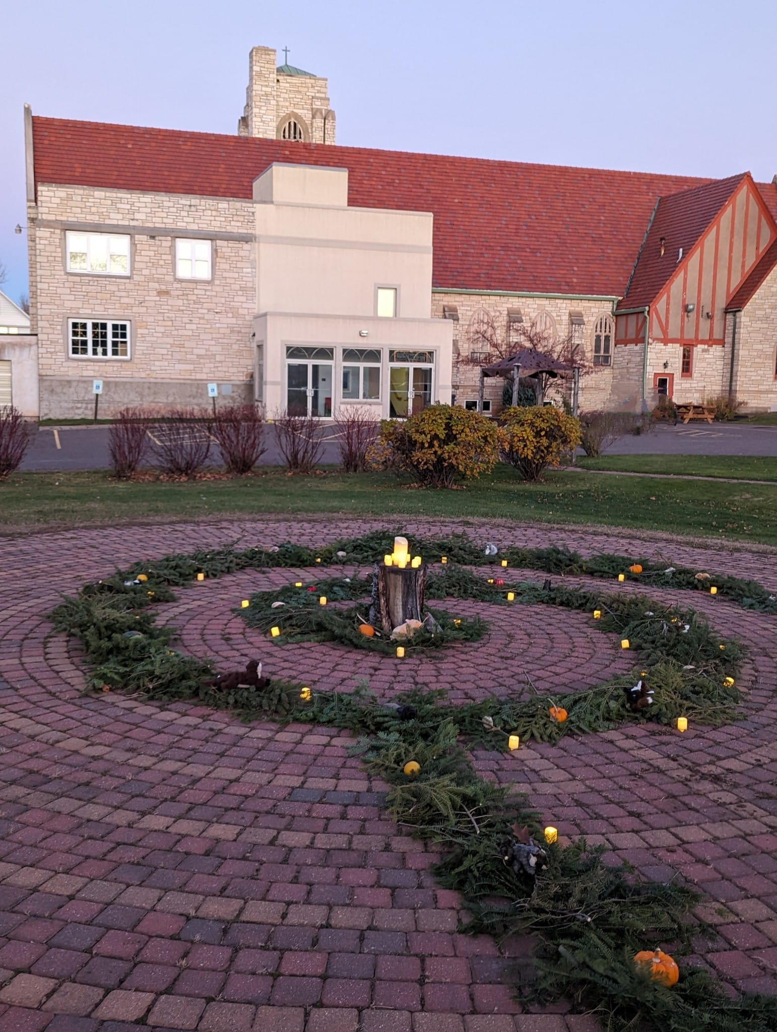 grass and brick labyrinth spiral on the ground, with tan building with red roof in background.