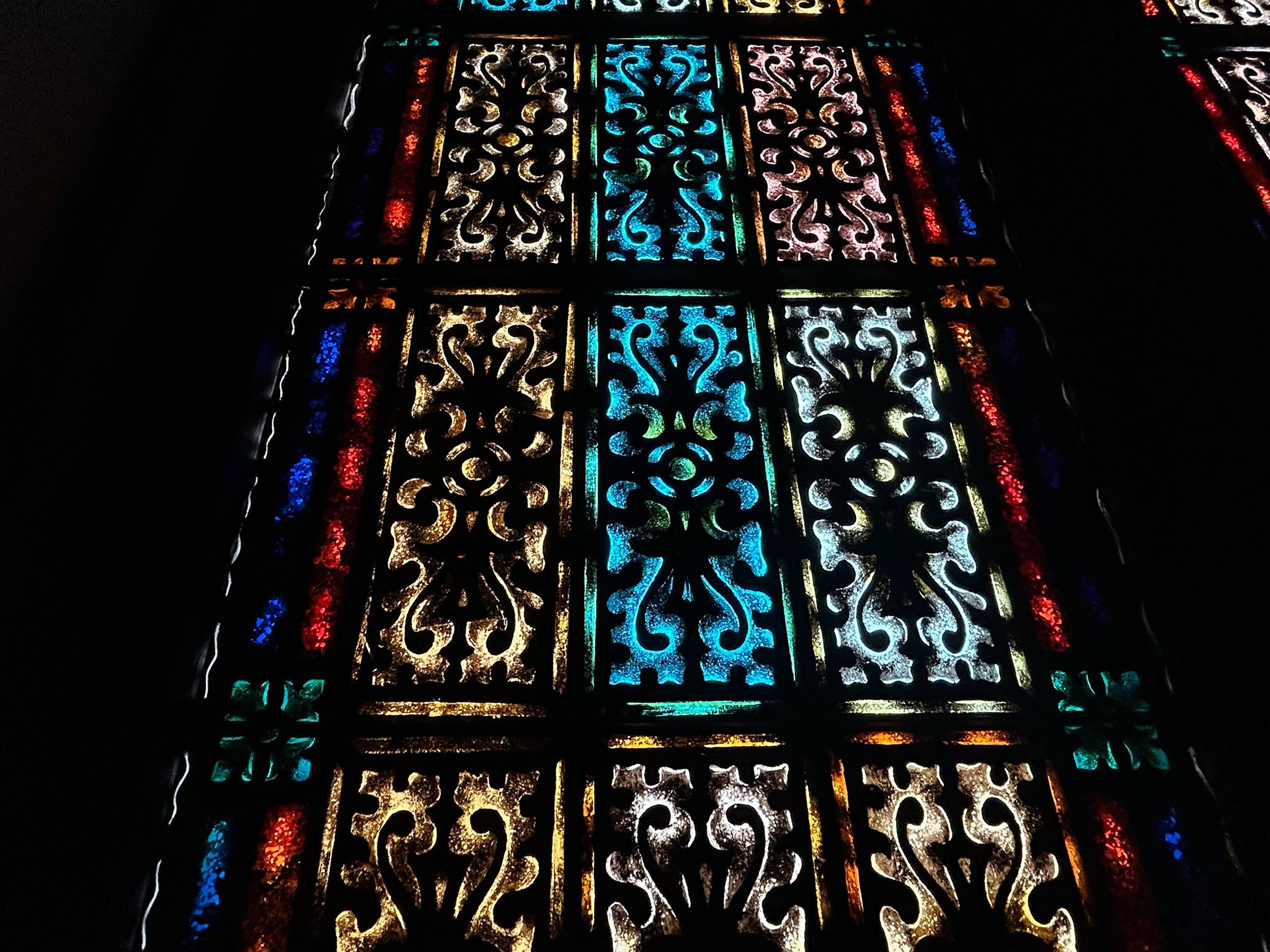 red, blue, teal, tan, pink, and black stained glass in abstract patterns.
