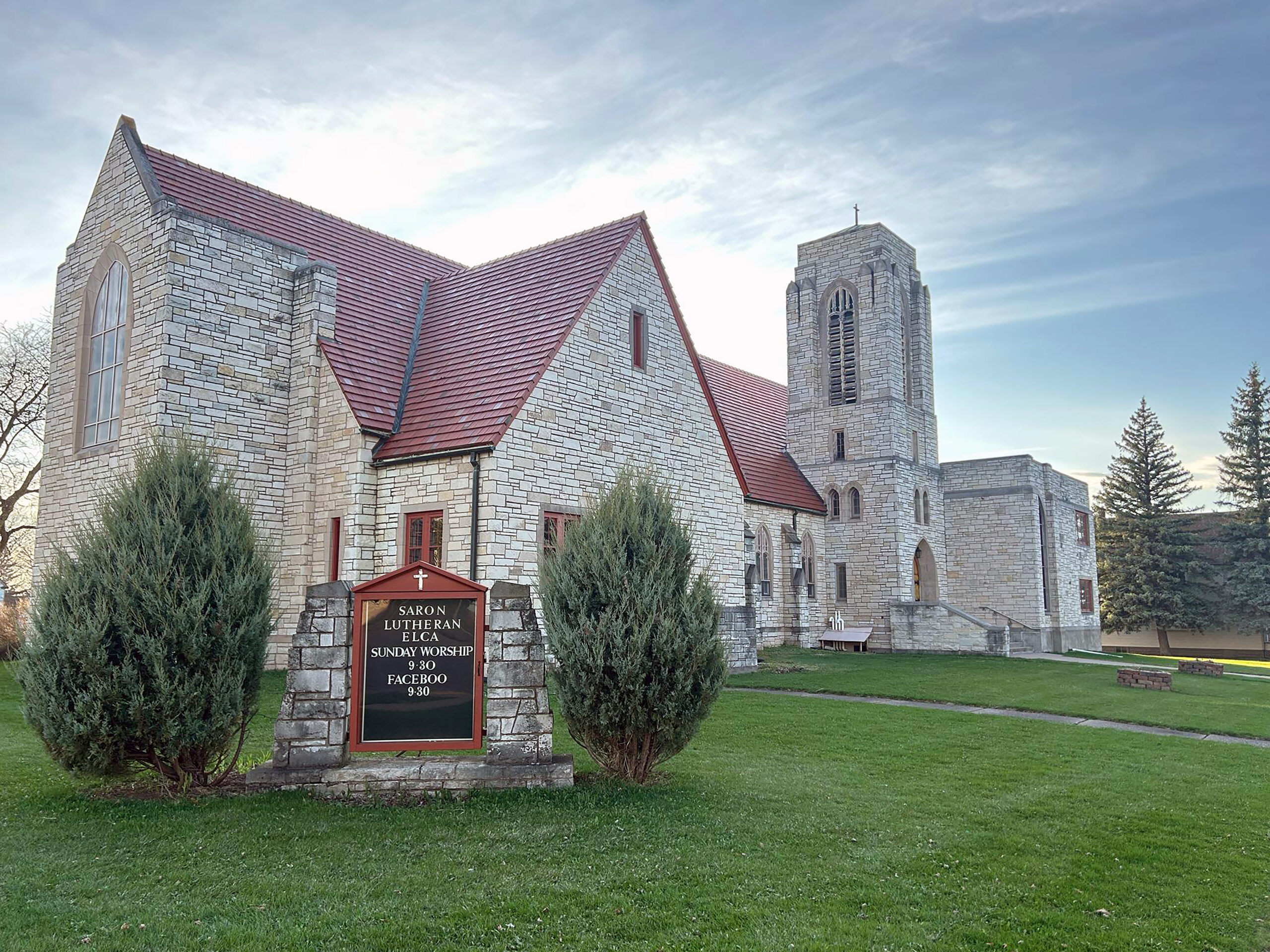 large brick building with red roof, tower, grass lawn, and sign that says Saron Lutheran Church.