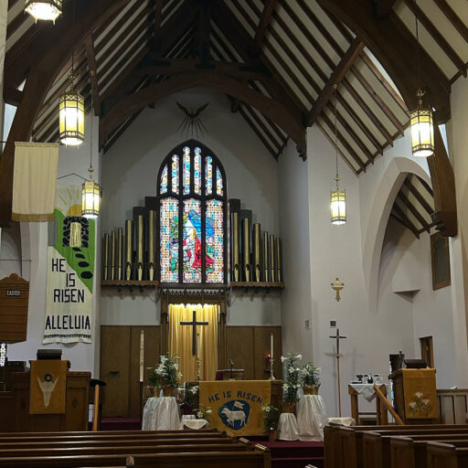pews, altar, cross, stained glass beneath soaring ceiling.