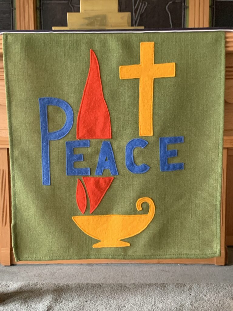 Green altar cloth with blue "Peace" yellow cross, red flame, and yellow bowl.