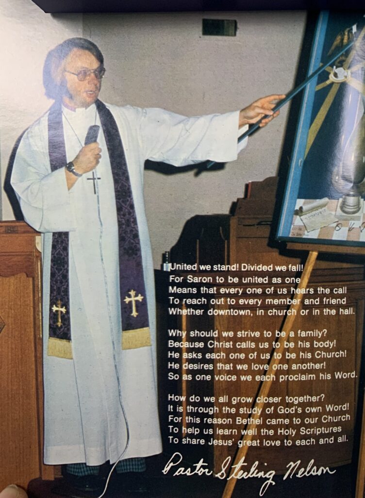 color photo of man holding microphone, wearing clerical white robe, purple stole with gold crosses, and pointing at an eisel. Some text on the photo.